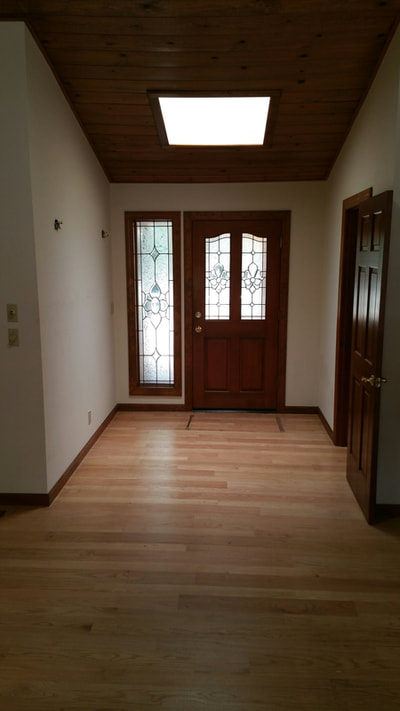 Dark and empty entry area into an older home with no lighting, no furnishings, drab walls and bare floors.